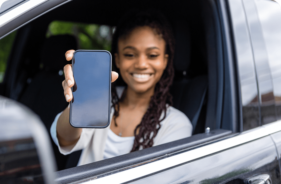 Woman in car holding smartphone, smiling.