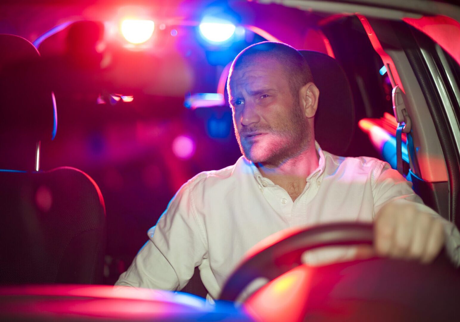 Man driving car with police lights flashing behind.