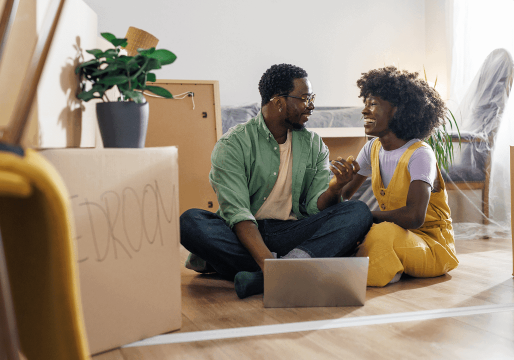 Couple sitting among moving boxes, smiling happily.